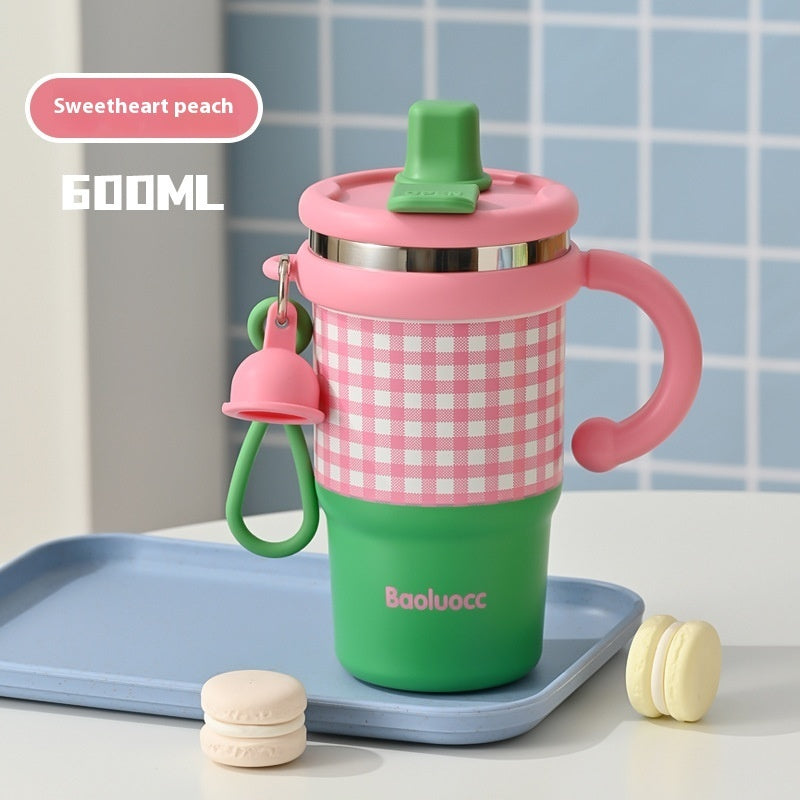 Green and pink sippy cup with checkered pattern on a blue tray against a tiled wall background.